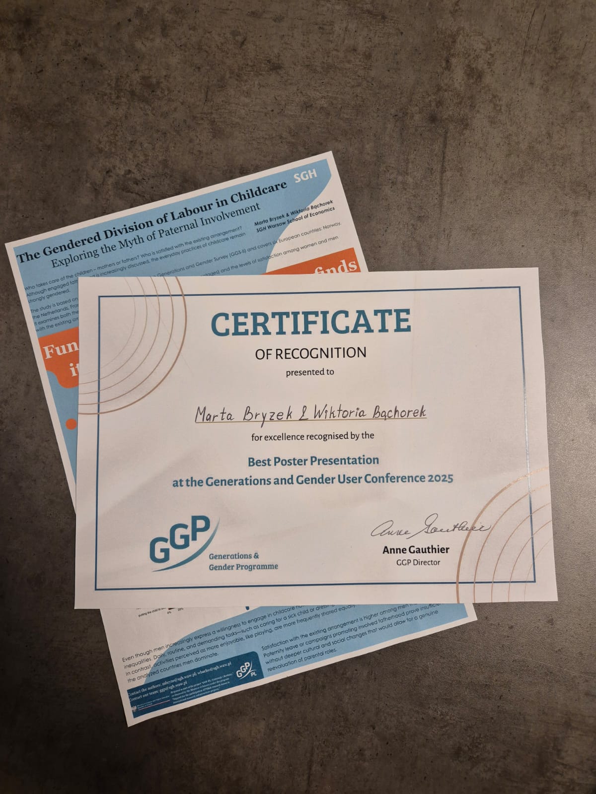 Zdjęcie certyfikatu wygranej za najlepszy plakat oraz mała wersja plakatu położona na stole pod nim